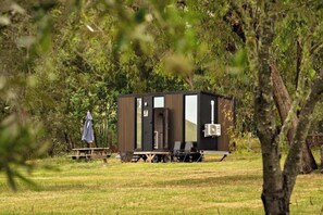 A small, modern cabin with a sliding door, a small porch, and a picnic table. - Olive Sanctuary by Tiny Away (Taggerty)
