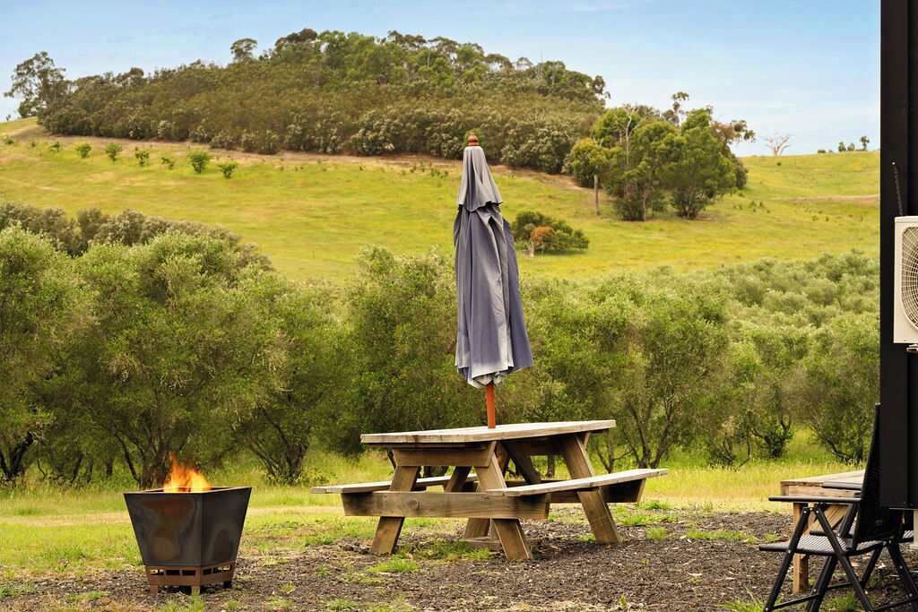 Un montaje para picnic con una fogata, una mesa de madera y una sombrilla en un área verde al aire libre.