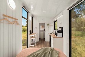 A compact, modern room with a bed, a small kitchenette, and a view of the outdoors. - Olive Sanctuary by Tiny Away (Taggerty)