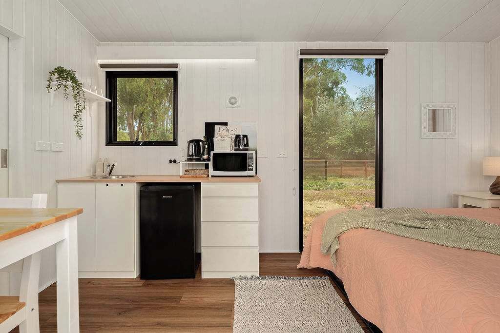A compact bedroom with a bed, a small kitchenette, and a sliding glass door leading to a garden.