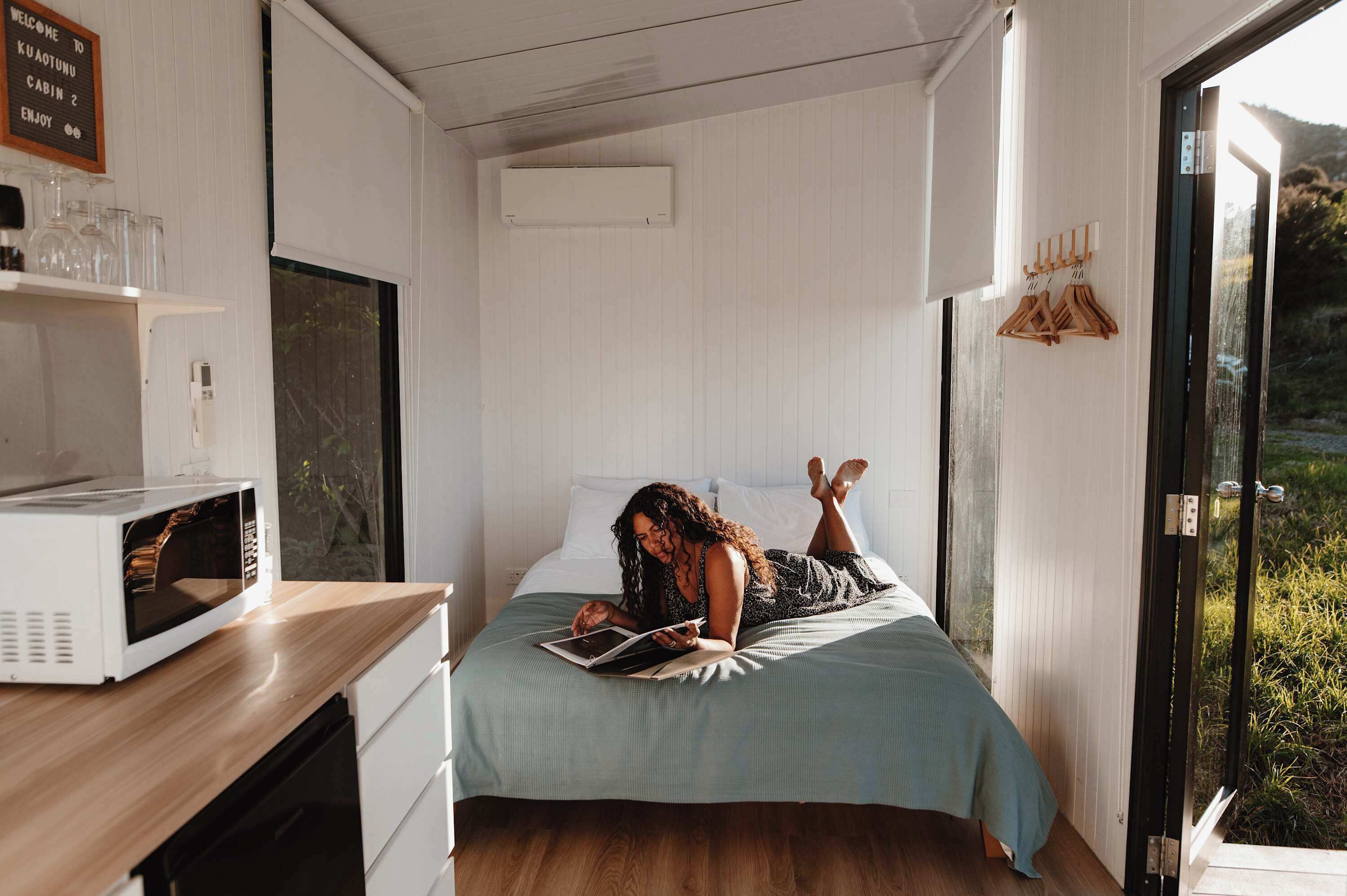 A bedroom with a bed, a microwave, a shelf with glasses, and a sign.