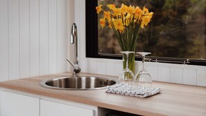 Una cocina con un lavamanos de acero inoxidable, un florero con flores amarillas y dos copas de vino sobre una encimera de madera.