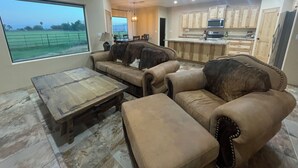 Un salon spacieux doté d’une grande fenêtre, d’un ventilateur de plafond et d’un coin cuisine avec des meubles en bois.