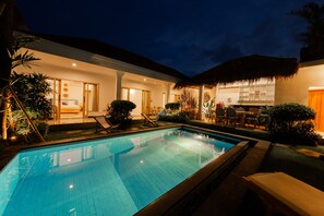 A swimming pool with lounge chairs, a bar area, and a thatched roof structure.