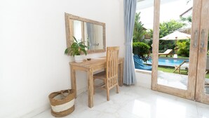 Een kamer met een houten bureau, een stoel, een spiegel, een kamerplant en uitzicht op een zwembad door een glazen deur.