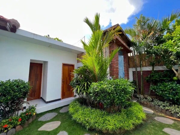 A two-story house with a white exterior, a wooden door, and a brick section. There is a well-maintained garden with various plants and a stone pathway.