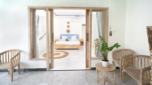 Een kamer met een bed, een klein tafeltje met een plant en twee houten stoelen.