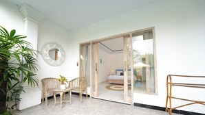 Een kamer met een bed, een klein tafeltje met stoelen, een spiegel en een glazen deur naar een andere ruimte.