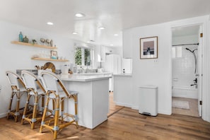 Ett modernt kök med vita köksskåp, en köksö och en matplats med stolar i rotting.