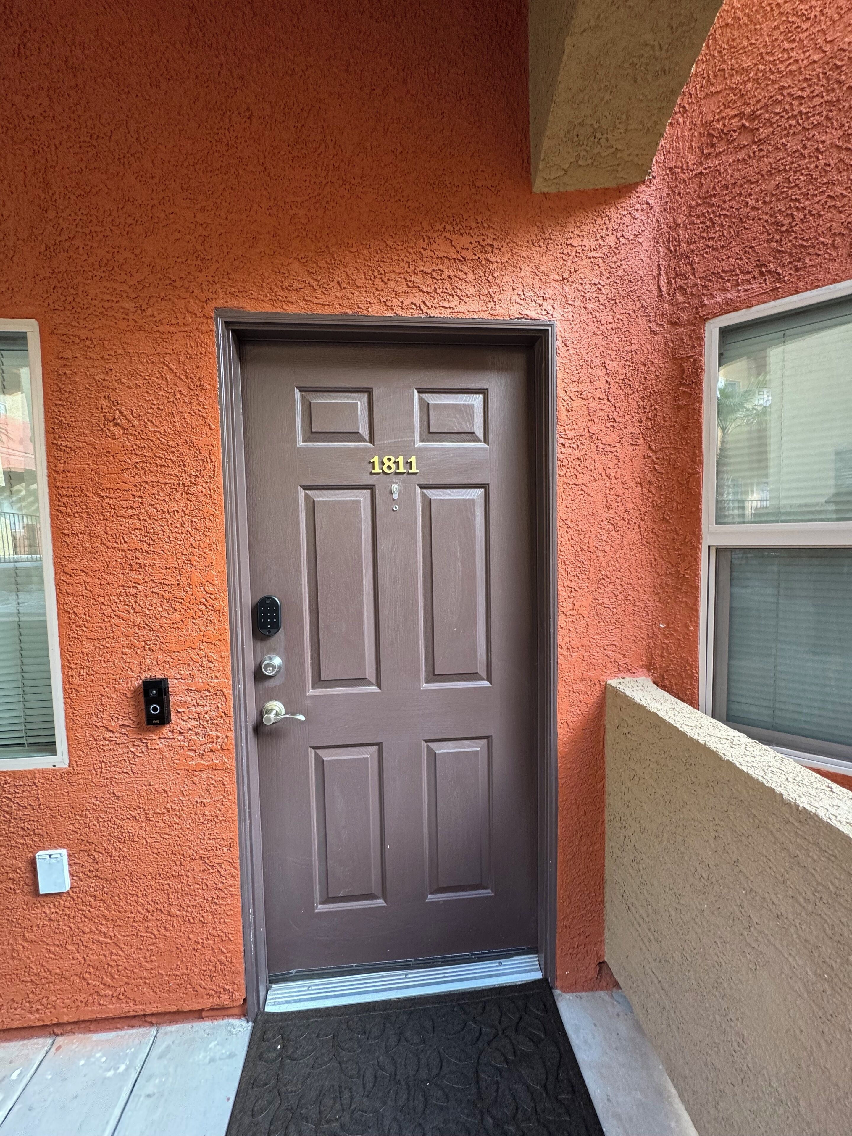 A brown door with the number 1811, a keypad lock, and a doormat.