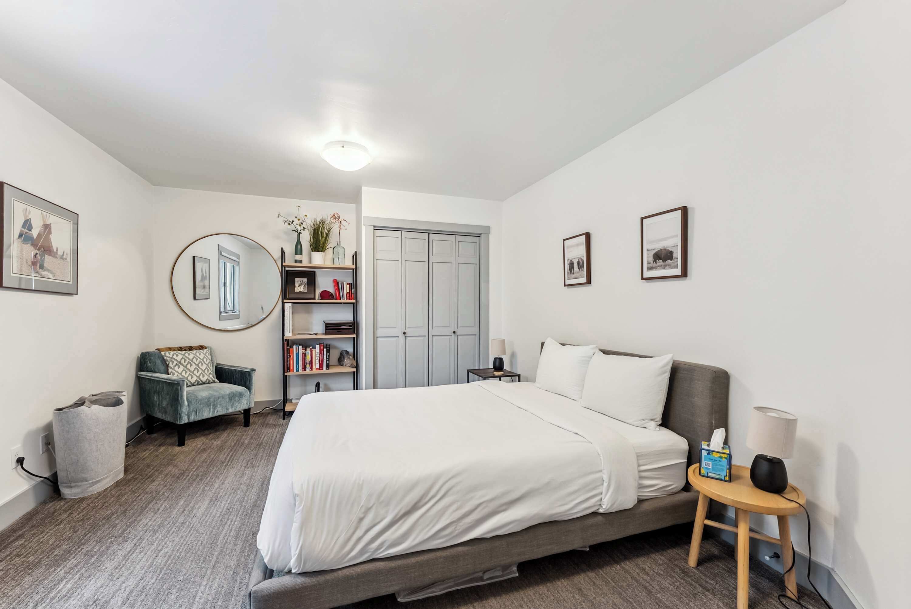 A bedroom with a bed, a chair, a bedside table, a lamp, a bookshelf, and a wardrobe.