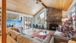 A living room with a stone fireplace, wooden ceiling, and a television displaying a snowy scene. - Breckenridge Mountain Retreat | Hot Tub & Views (Breckenridge)