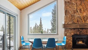 A modern interior with a large window, a stone fireplace, and blue chairs around a glass table. - Breckenridge Mountain Retreat | Hot Tub & Views (Breckenridge)