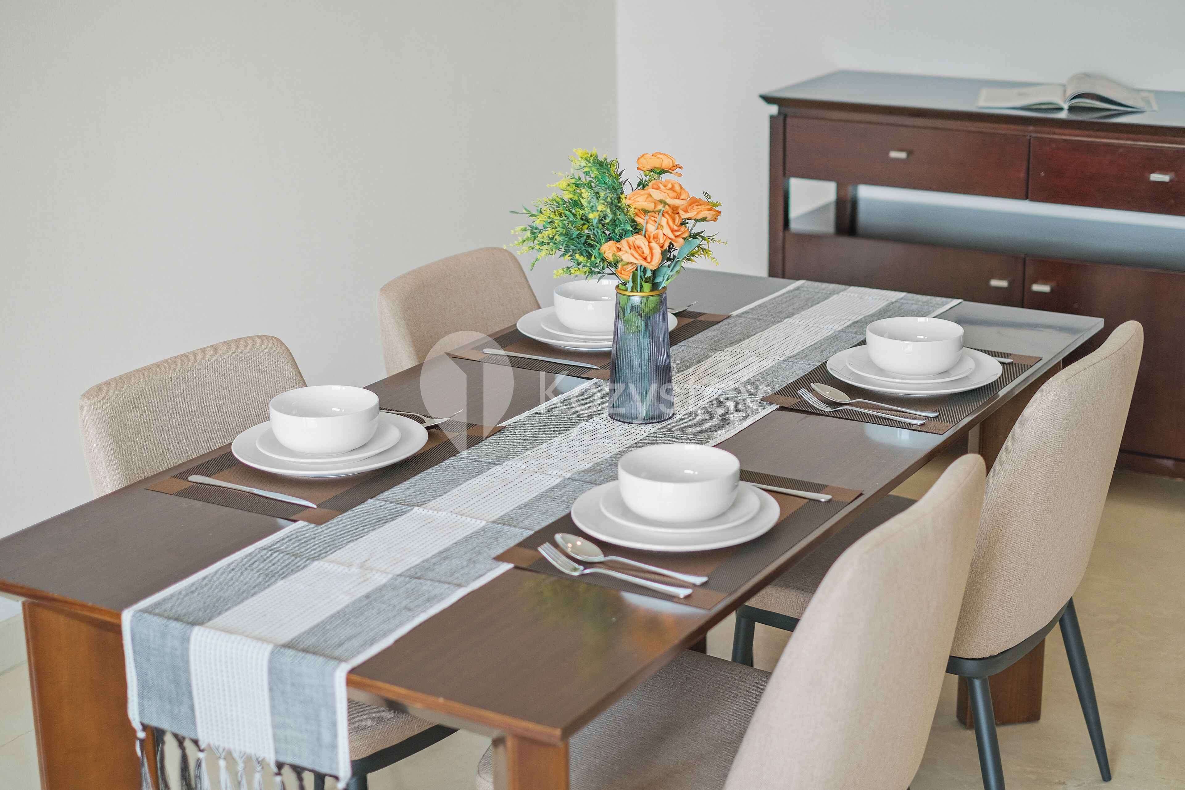A dining table set with white plates, bowls, and cutlery, a vase with flowers, and a placemat.
