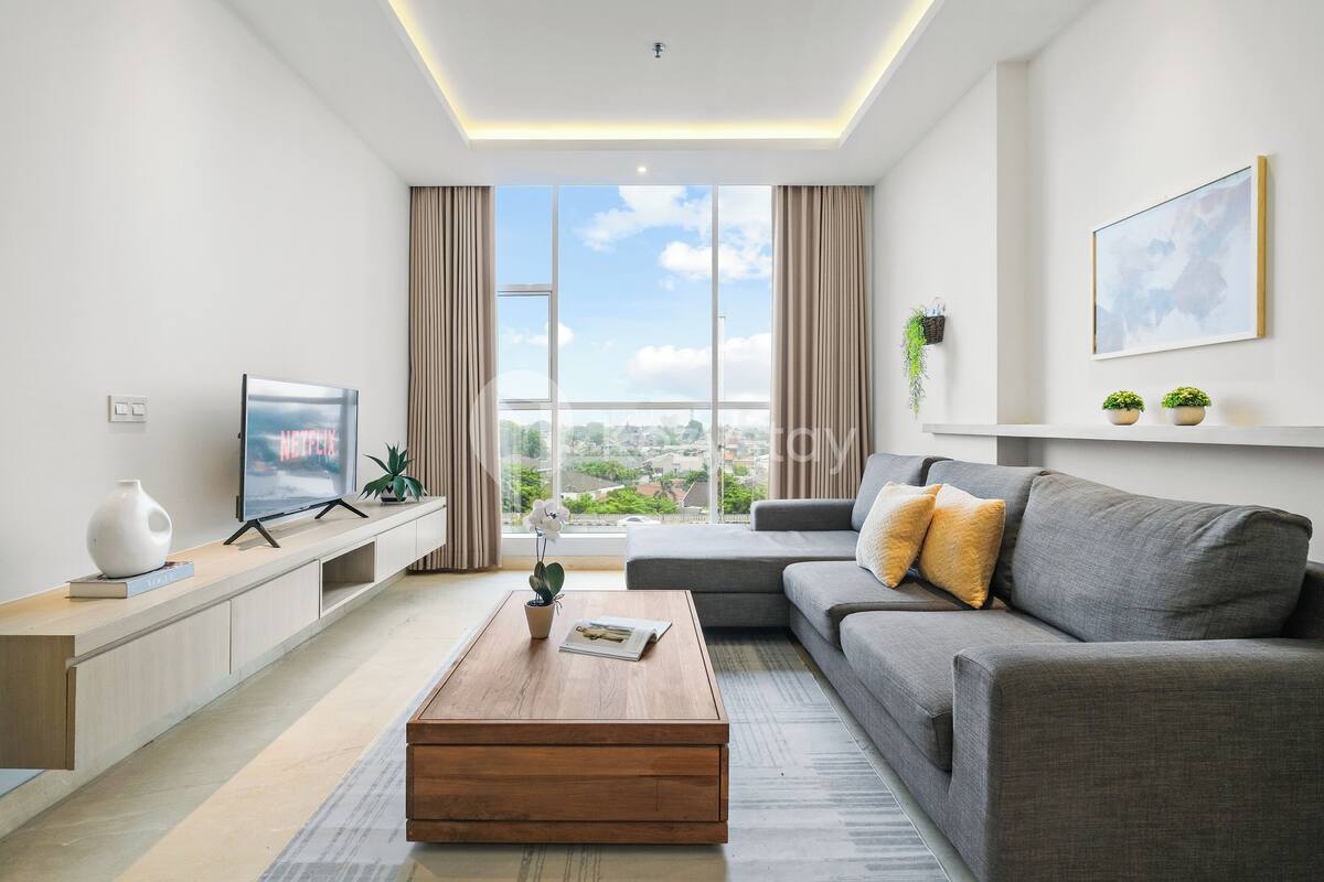 Una sala de estar moderna con un sofá gris, una mesa de centro de madera, un televisor y un ventanal con vistas a la ciudad.