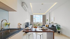 Una cocina moderna con una isla central, taburetes blancos de bar y una mesa de comedor con cuencos y frutas.