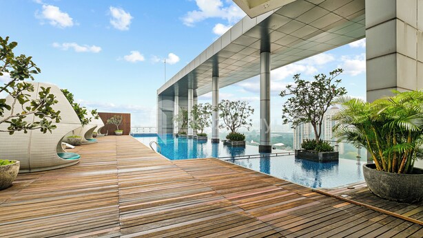Un área de piscina moderna en la azotea con terraza de madera, rodeada de plantas en macetas y un cielo despejado.