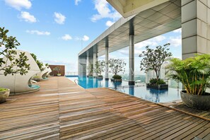 Un área de piscina moderna en la azotea con terraza de madera, rodeada de plantas en macetas y un cielo despejado.