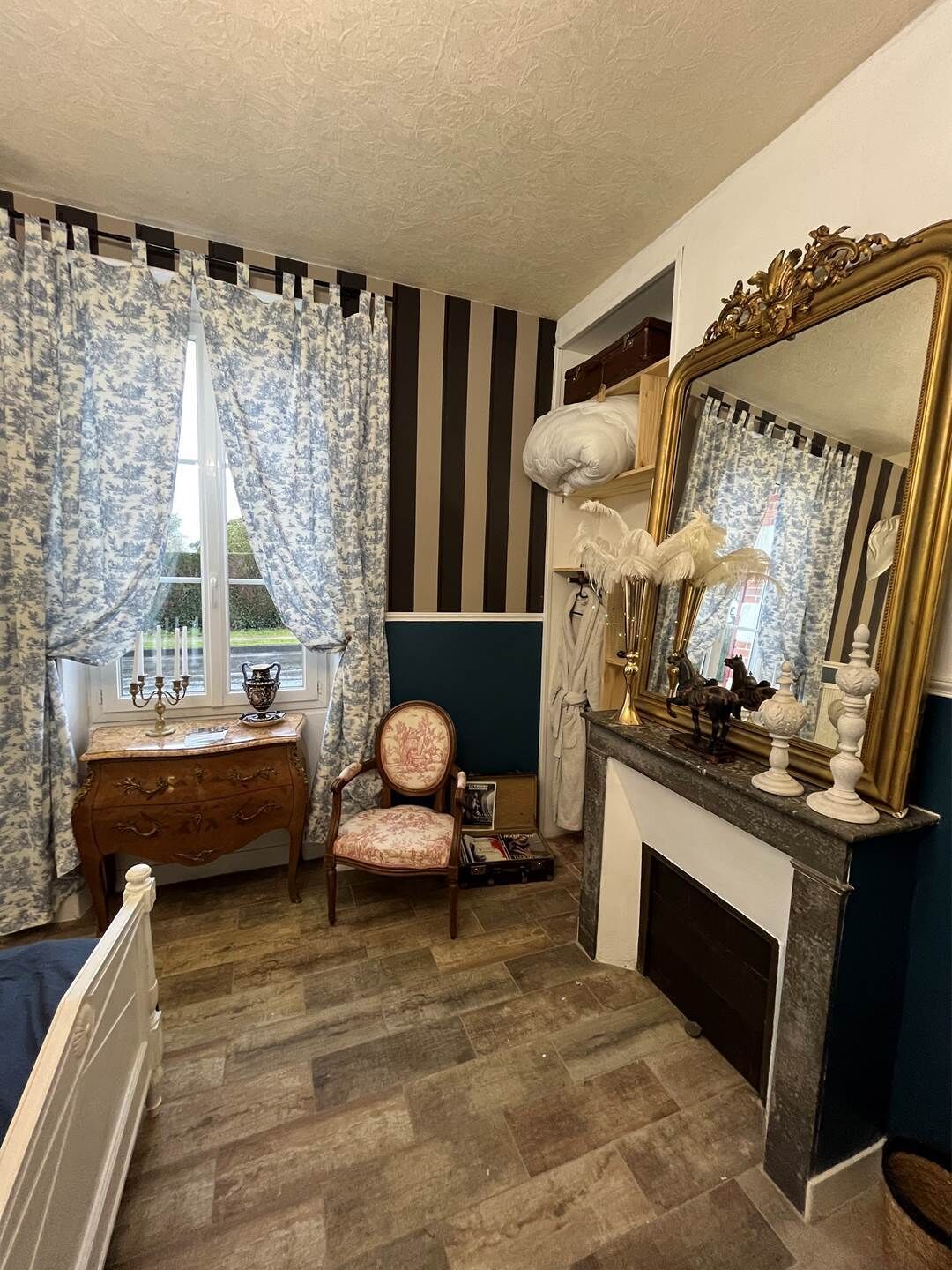 A room with a wooden dresser, a chair, a large mirror, and a fireplace.