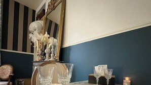 Un tavolo da pranzo con bicchieri trasparenti e piatti, uno specchio decorativo e una candela su una parete blu e bianca.