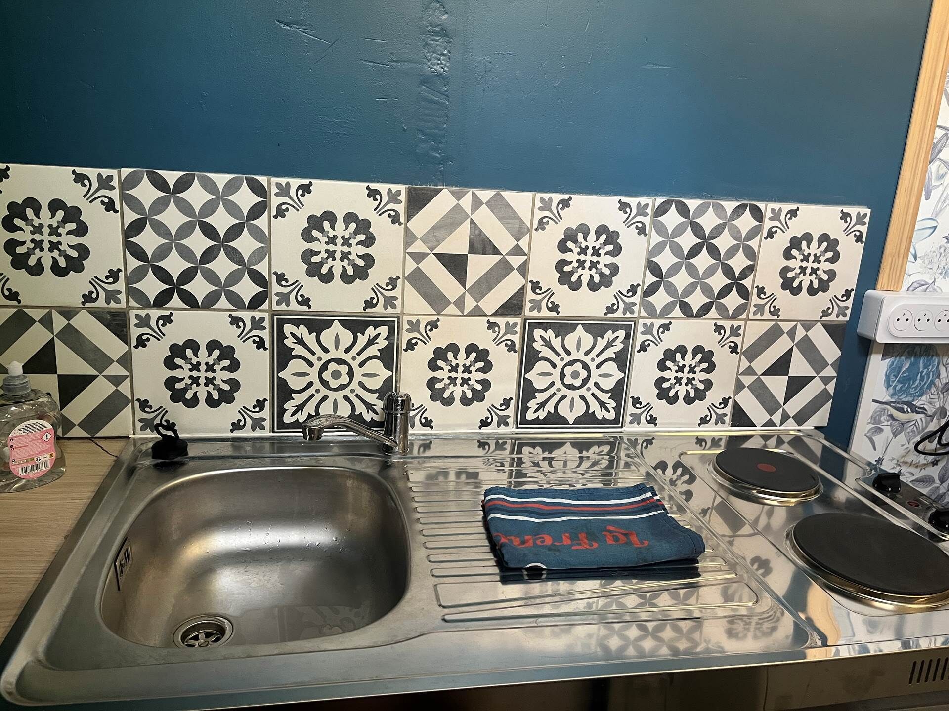 A kitchen with a stainless steel sink, a patterned backsplash, and a towel on the counter.