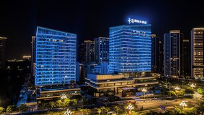 A modern hotel with a prominent blue-lit facade, multiple floors, and a visible entrance area with a covered walkway. - THE MORDIN HOTEL (Guangzhou)