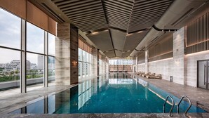 An indoor swimming pool with clear views of the cityscape through large windows. - THE MORDIN HOTEL (Guangzhou)
