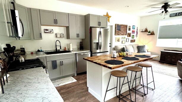 A modern kitchen with grey cabinets, a stainless steel refrigerator, and a wooden island with bar stools.
