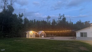 A house with a large deck, a covered area with string lights, and a grassy yard.