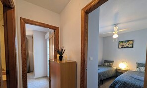 Ein Schlafzimmer mit zwei Betten, einem Deckenventilator, einem Nachttisch mit Lampe und einem Bild an der Wand.