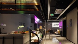 Un moderno vestíbulo de hotel con una recepción, una vitrina con aperitivos y un letrero de neón que dice "SOMET INTEREST".