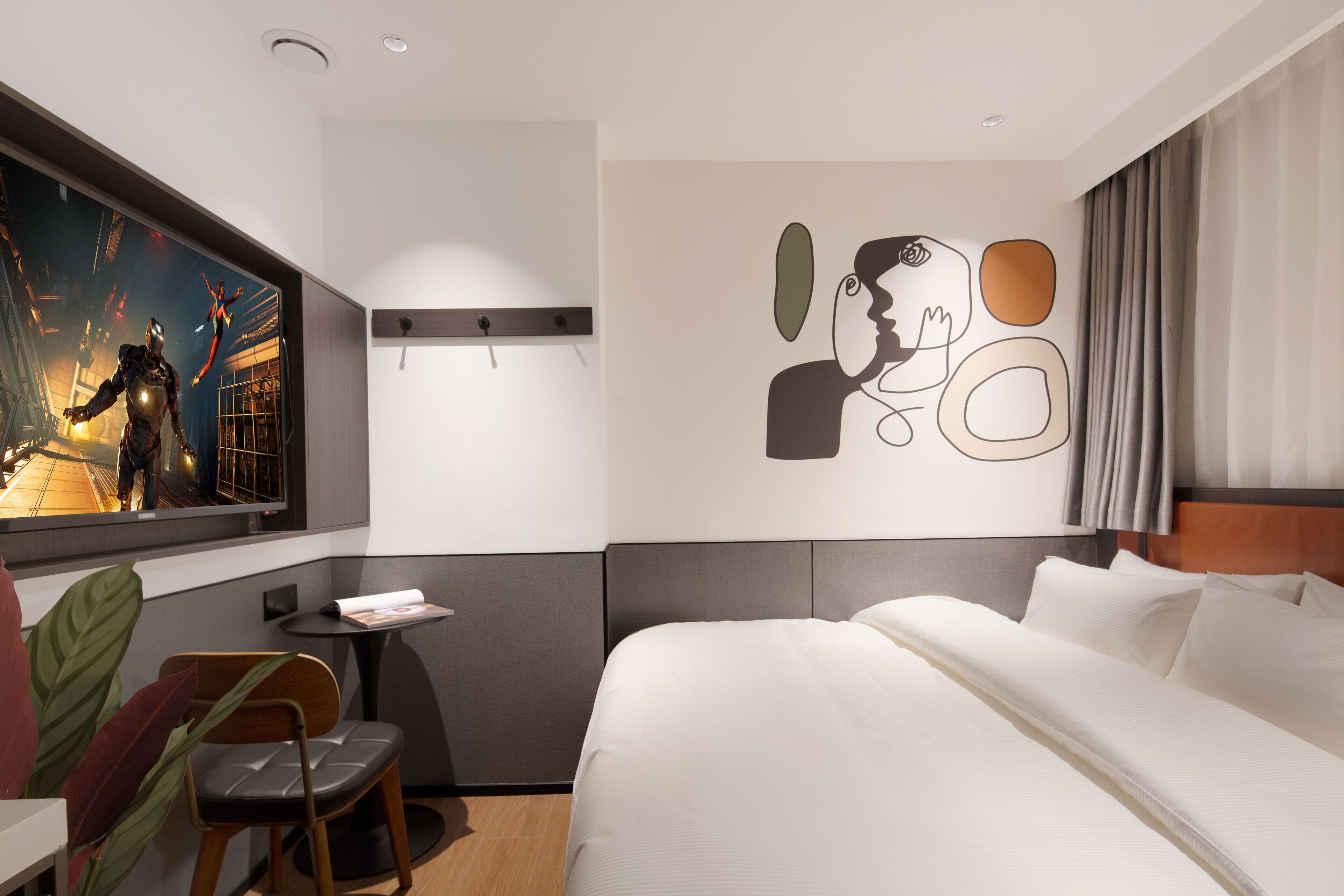 A modern hotel room with a large bed, a small desk, a chair, and a wall art piece.