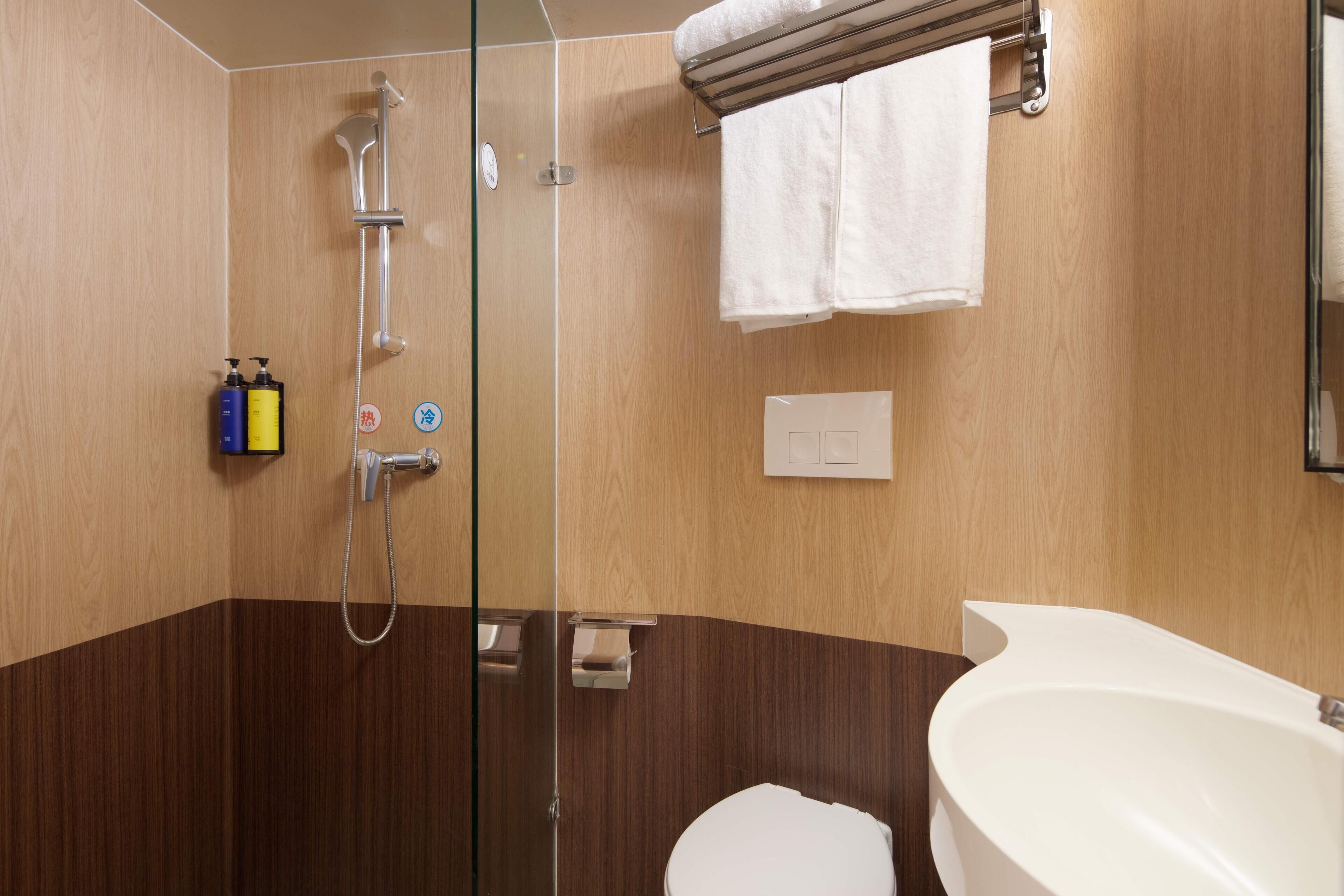 A modern bathroom with a glass shower enclosure, a white bathtub, and wooden paneling.