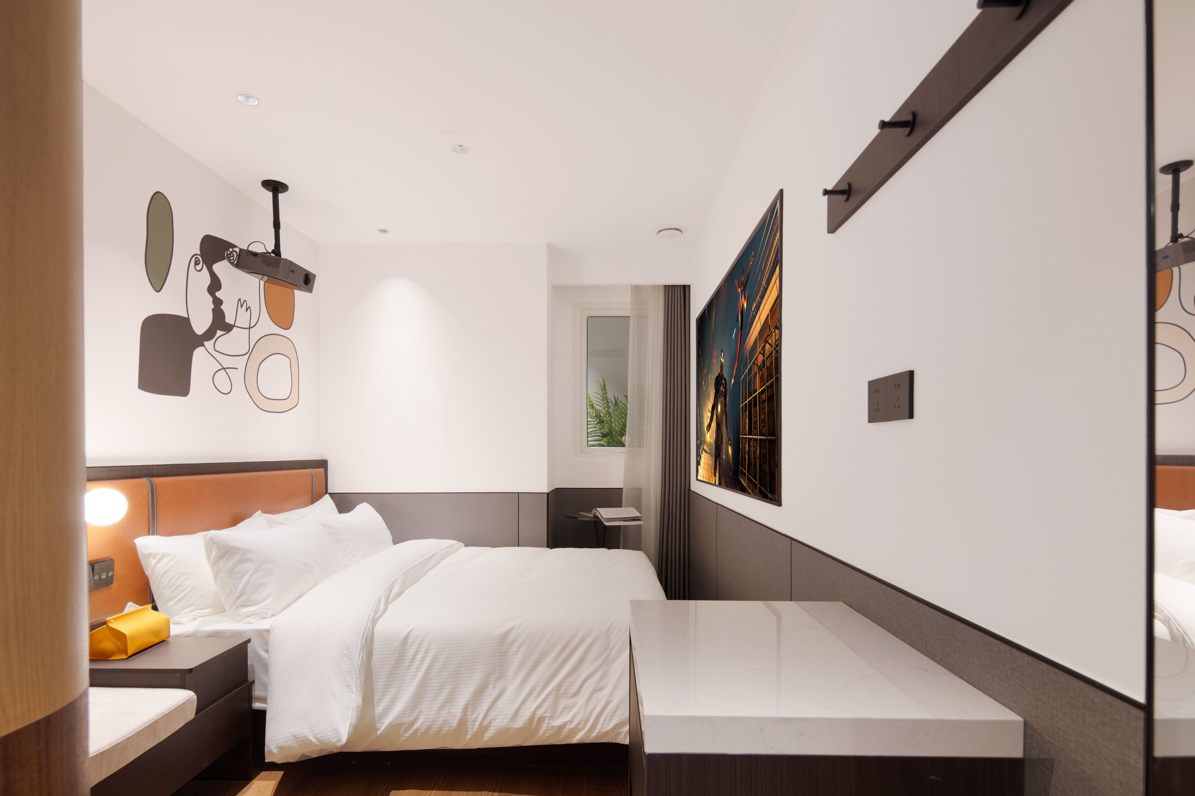 A modern hotel room with a large bed, bedside table, and a desk.