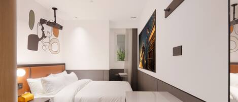 A modern hotel room with a large bed, bedside table, and a desk.