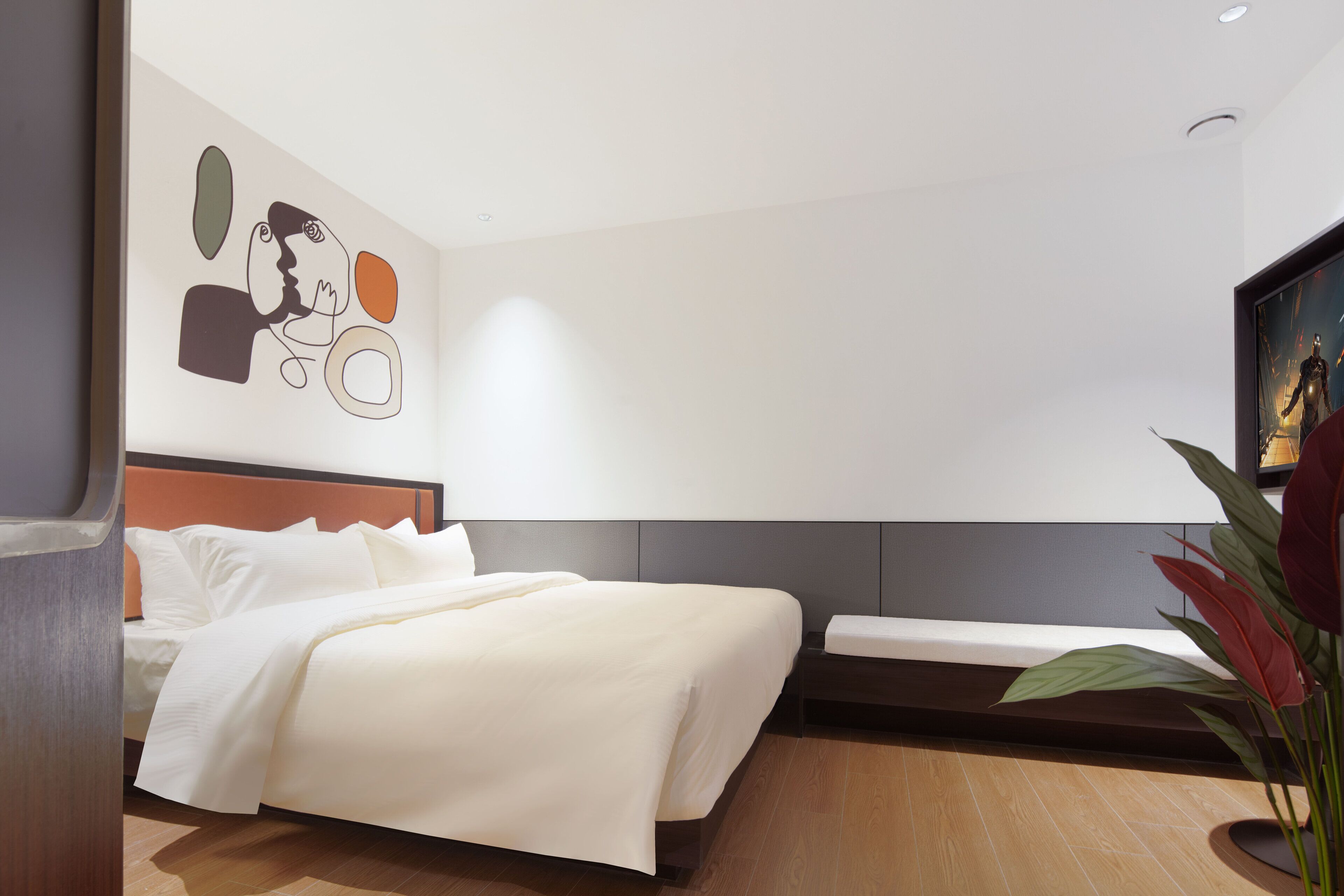 Een moderne hotelkamer met een groot bed, een nachtkastje, een aan de muur bevestigd kunstwerk en een potplant.