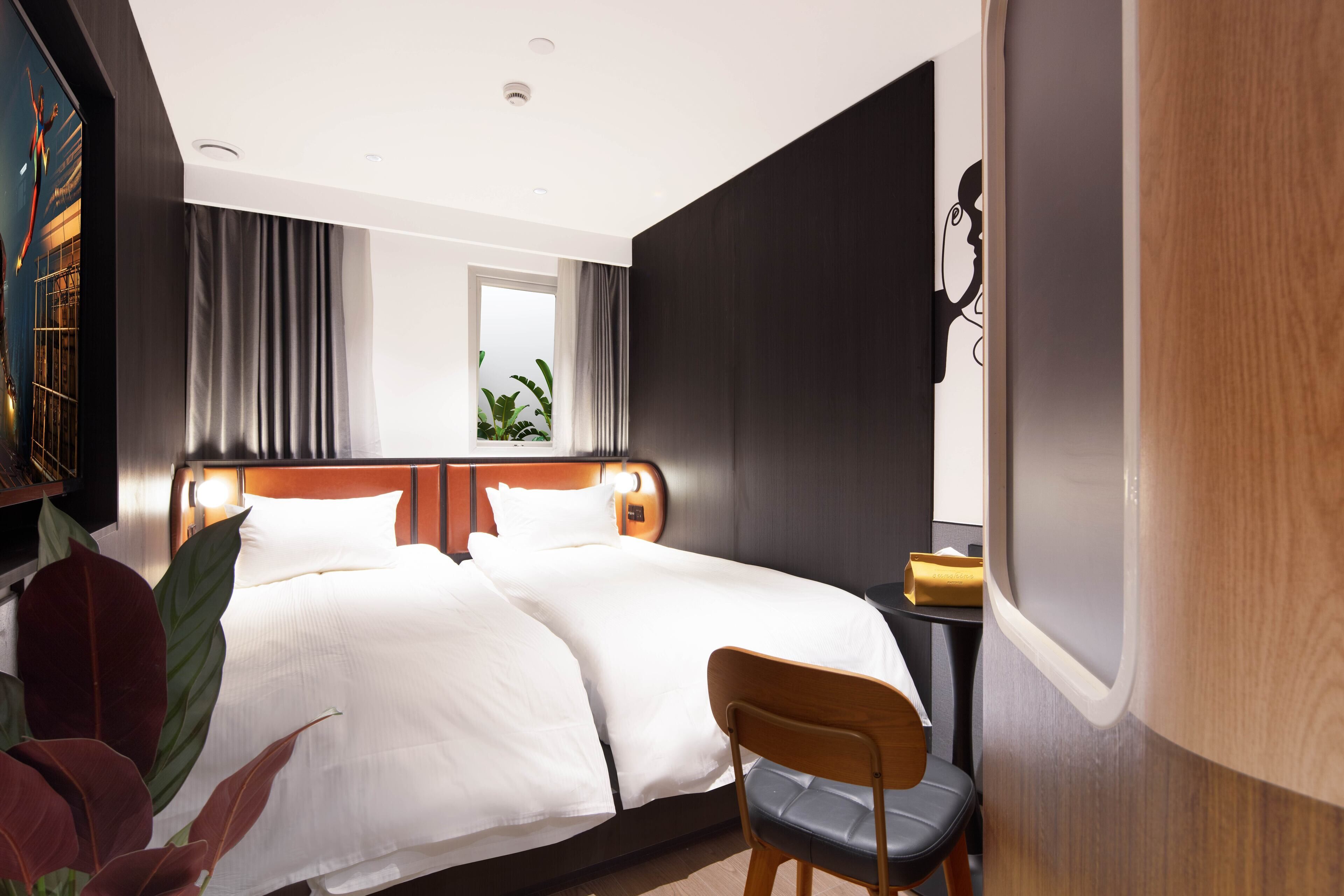 A modern hotel room with a large bed, a wooden headboard, a desk with a chair, and a large window with curtains.