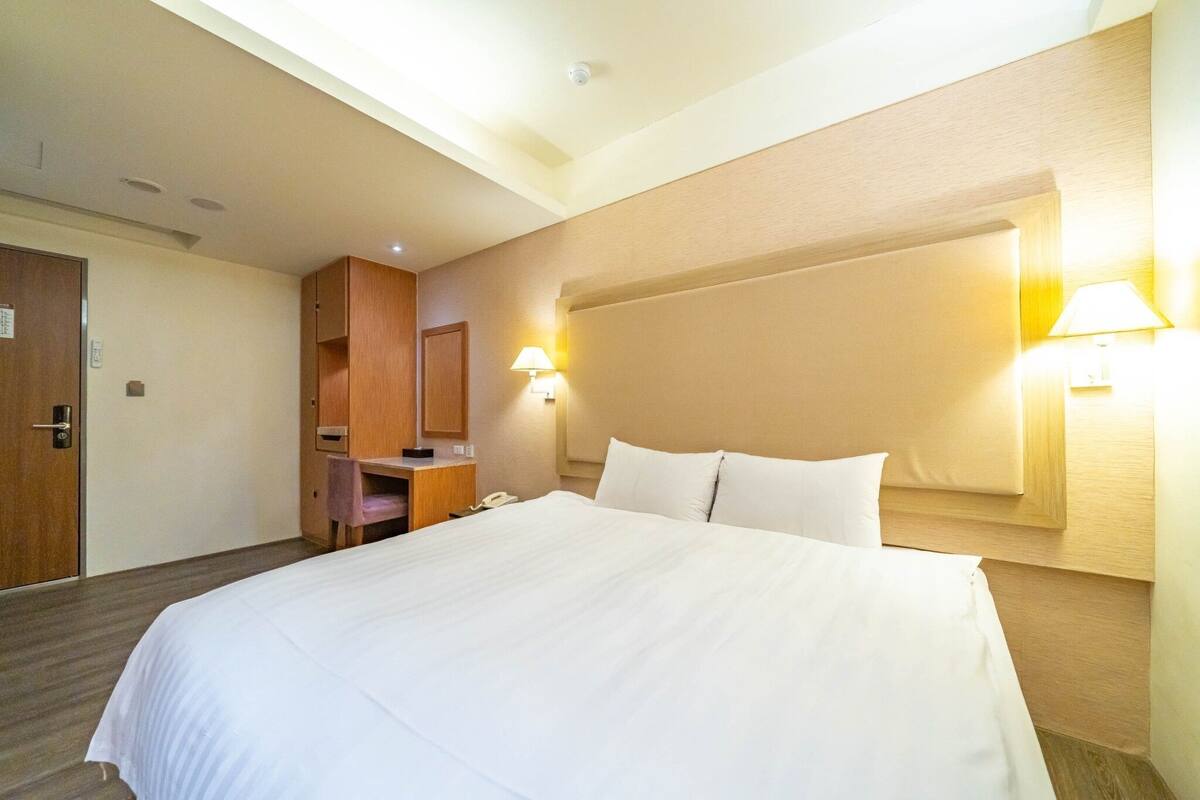 Ein Hotelzimmer mit einem großen Bett, einem Schreibtisch mit Lampe, einem Kleiderschrank und einem Spiegel.