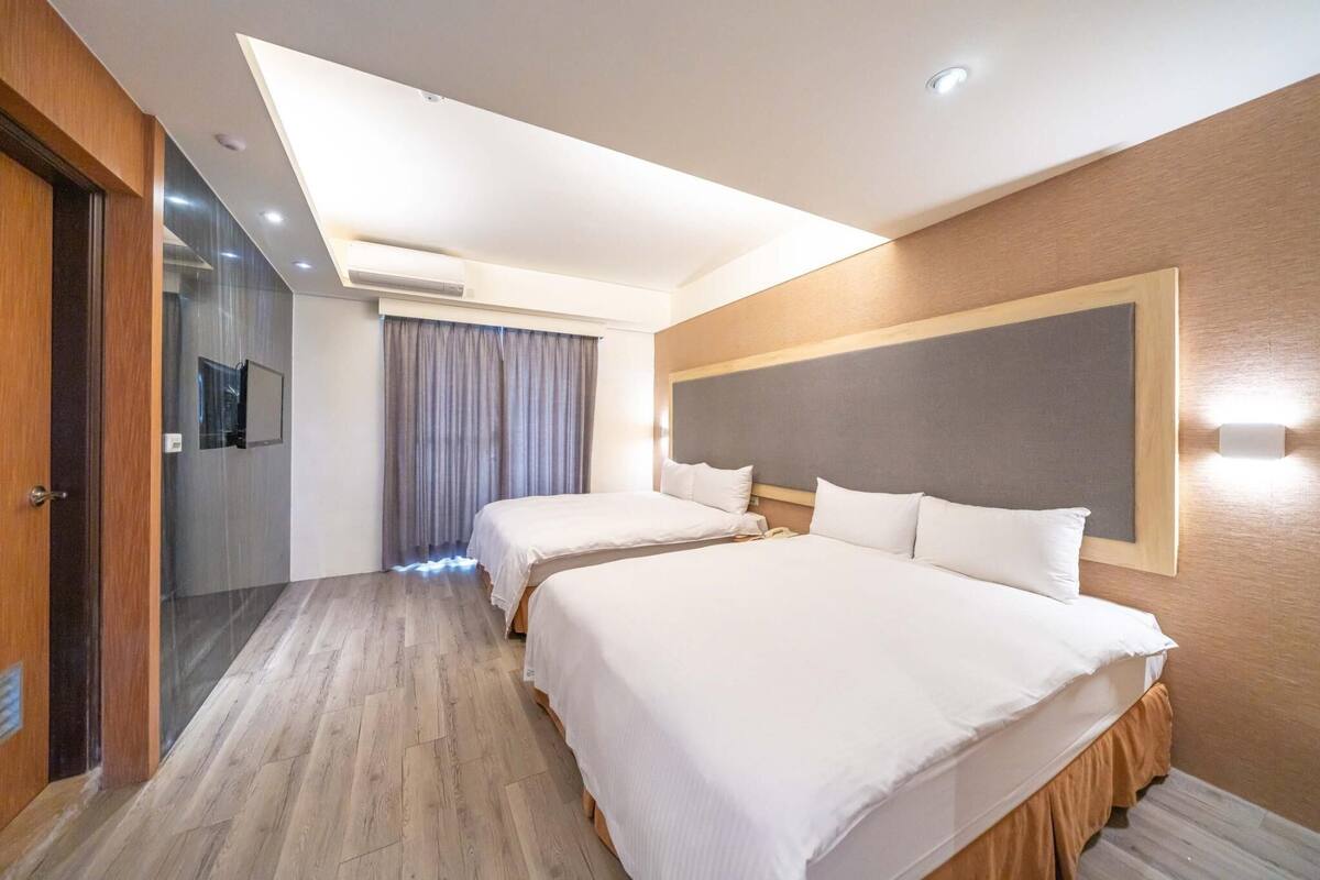 Ein Hotelzimmer mit zwei Betten, einem großen Spiegel, einem Flachbildfernseher und einer Deckenleuchte.
