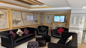 Un salon moderne avec des canapés noirs, des poufs et un téléviseur.