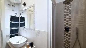 A bathroom with a white sink, a mirror, a towel rack, and a shower area with a tiled wall.