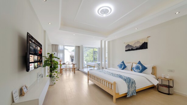 A modern hotel room with a large bed, a TV mounted on the wall, a desk, and a plant. - Villa in the park (Guiyang)