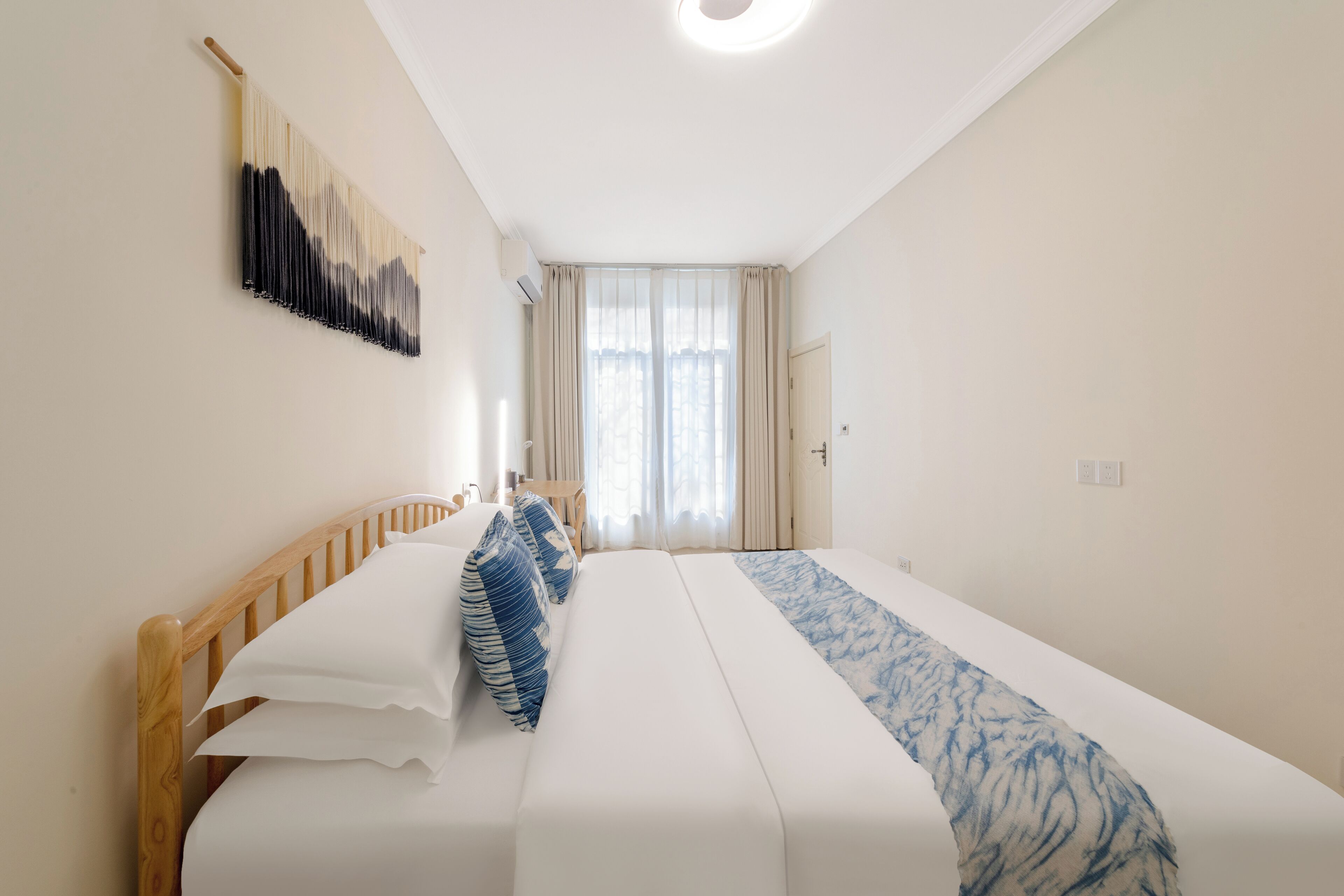A neatly arranged hotel room with a large bed, a wooden headboard, a wall-mounted artwork, and a window with curtains.