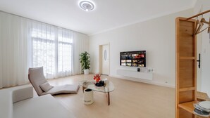 A modern living room with a glass coffee table, a sofa, a chair, and a TV mounted on the wall. - Villa in the park (Guiyang)