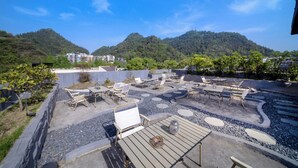 An outdoor patio area with seating and tables, surrounded by a landscaped garden and a view of hills. - Villa in the park (Guiyang)