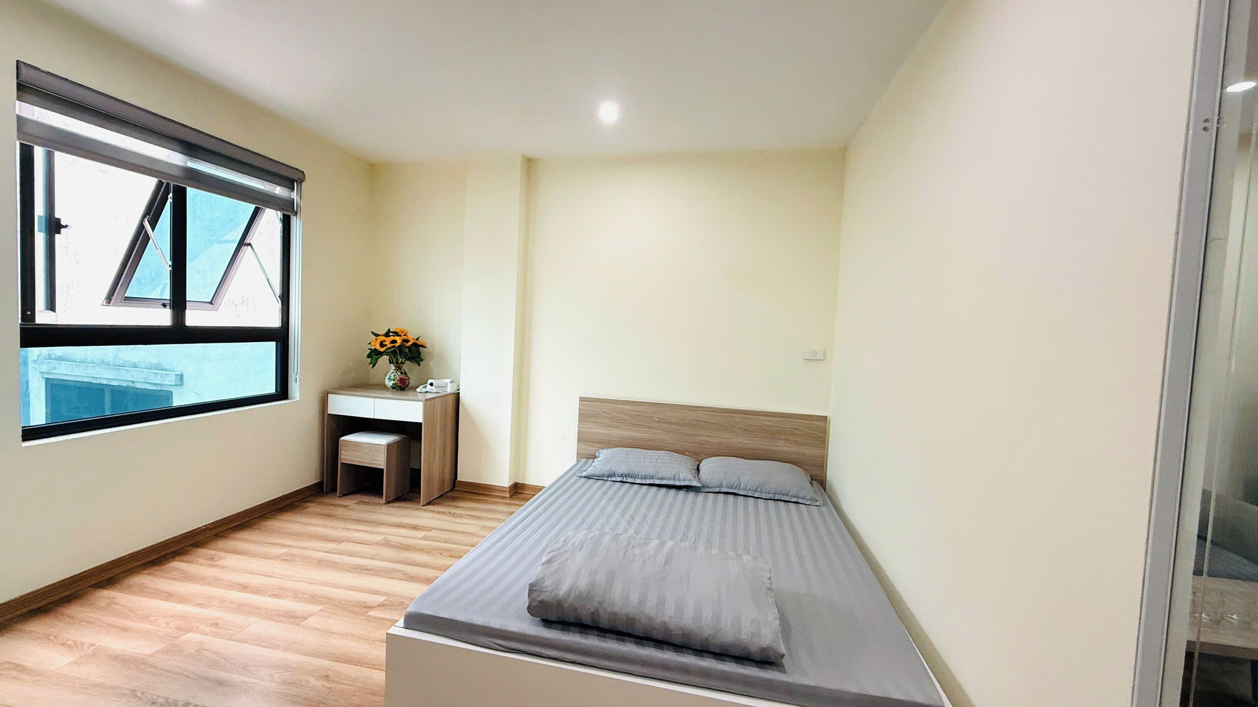 Een kleine slaapkamer met een bed, een bureau met stoel en een raam.