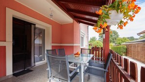 Une terrasse extérieure avec une table et des chaises en verre, un pot de fleurs suspendu et une clôture en bois.
