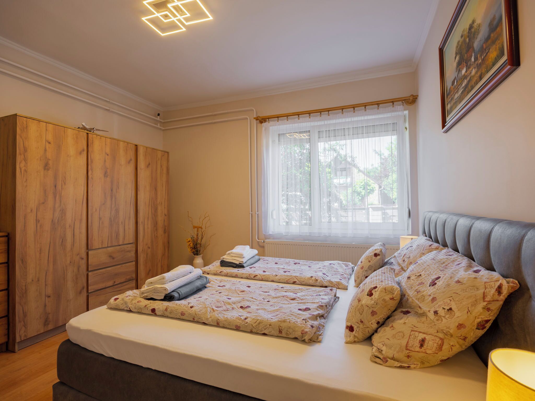 A bedroom with a bed, a wardrobe, a window with curtains, and a painting on the wall.