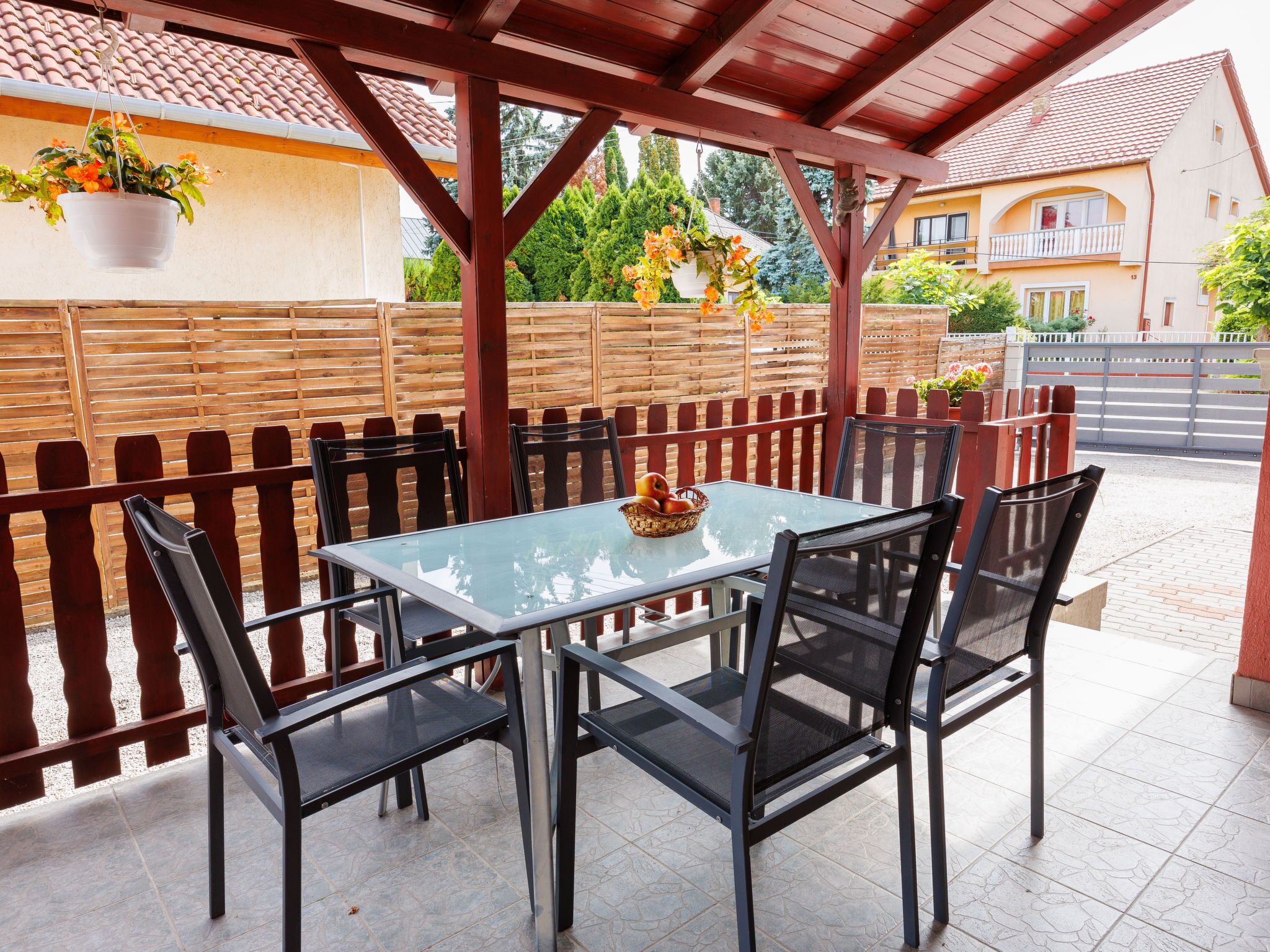 A covered patio with a glass table and black mesh chairs, surrounded by a wooden fence and a tiled floor.