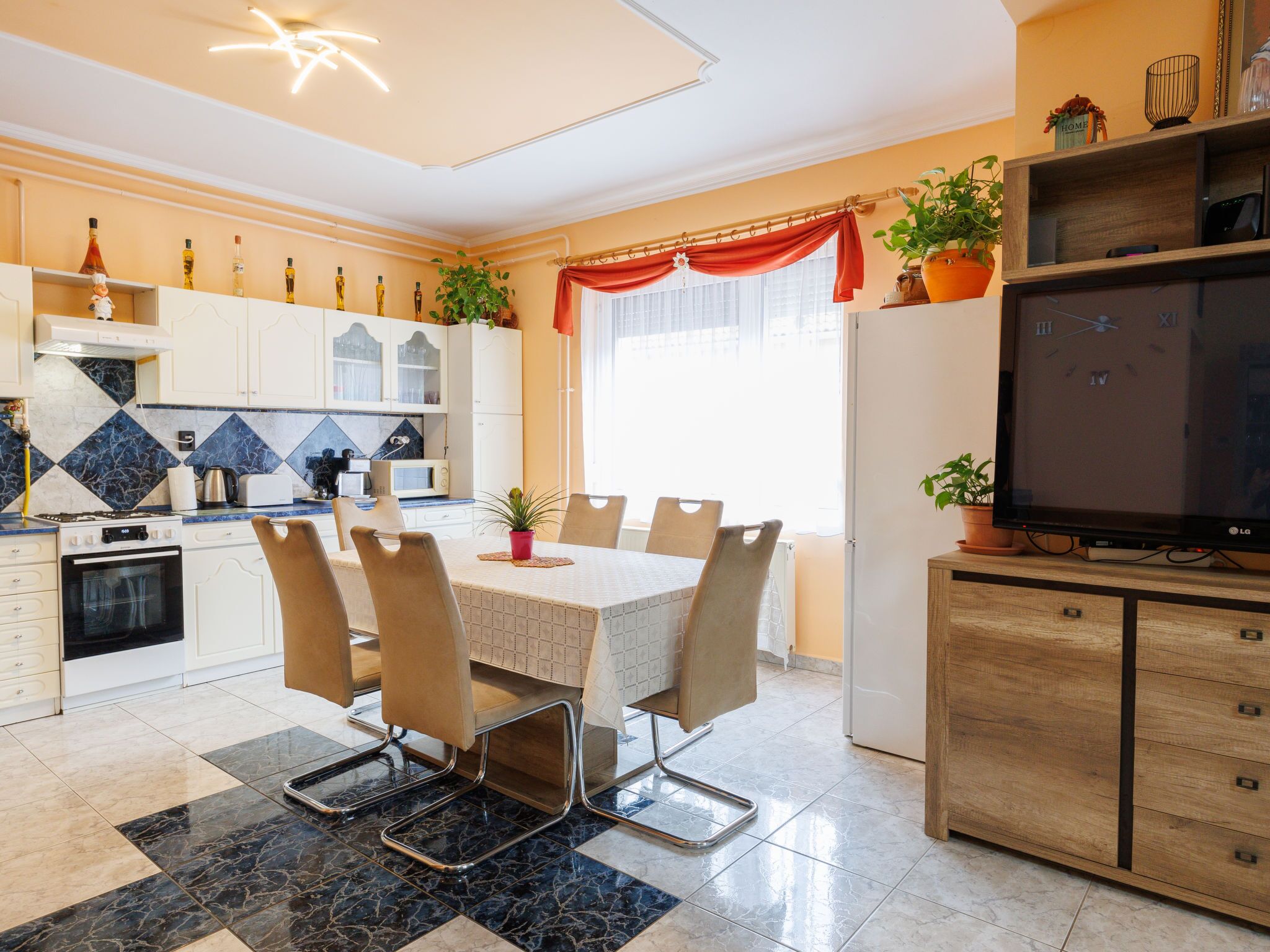 Una cocina moderna con comedor, que incluye una isla central, armarios blancos y un televisor de pantalla plana grande.